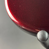 Close-up of a glossy dark red metallic surface with fine glitter, showing a curved edge and a small portion of a black cylindrical object against a gray background.