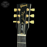 Close-up of a Gibson Les Paul Standard acoustic guitar headstock, featuring gold tuning pegs, gold 'Gibson' script, and 'Les Paul Model' branding on a black background.