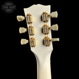 Close-up of the headstock of a white electric guitar, showing six gold-toned tuning keys with cream-colored tuning pegs against a solid black background.