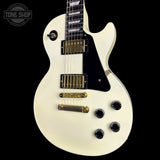 A white electric guitar with gold hardware and a black pickguard, photographed against a solid black background. A Tone Shop watermark is visible in the top-left corner.