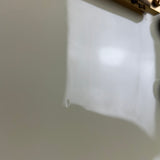 A close-up of a glossy white surface with a small circular defect or hole visible near the lower-left area, under warm lighting with a soft shadow cast to the right.