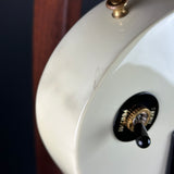 Close-up of a cream-colored guitar body showing a black and gold volume/toggle switch and a small scratch on the glossy finish.