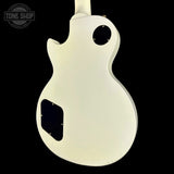 The back view of a white electric guitar body, featuring a double-cutaway shape, a circular hole near the top, and a black pickguard, shown against a solid black background with a Tone Shop watermark in the upper left.