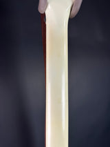 A close-up of a glossy, cream-colored cylindrical product, likely a candle stick or decorative tube, held vertically by hands at the top against a dark gray background.