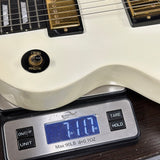 Close-up of an off-white electric guitar body resting on a digital scale showing 7.17 lbs, with the guitar pickups and strings visible against a dark wood surface.