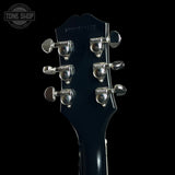 Close-up of the headstock of a dark blue Gibson electric guitar against a solid black background, showing six silver tuning pegs and the Gibson logo.