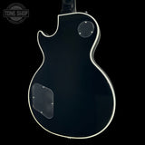 The back of a black electric guitar with a white binding edge, shown against a solid black background. A Tone Shop watermark is visible in the top-left corner.