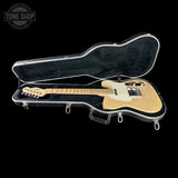 A natural wood electric guitar inside an open black hard case with white trim, photographed against a solid black background. A Tone Shop watermark is visible in the top-left corner.