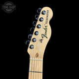 Close-up of a Fender Telecaster electric guitar headstock in natural wood, showing six black tuning pegs and the Fender Telecaster logo, set against a solid black background.