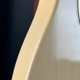 Close-up of a glossy light cream or natural wood guitar body edge with a small visible imperfection or scratch on the finish, against a dark background.