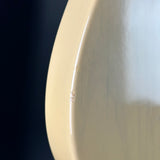Close-up of a glossy cream-colored wooden product surface with a small visible scratch on the left side, set against a dark background.