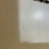 A close-up of a light beige or off-white textured surface with visible scratches, scuffs, and dust, likely a tabletop, panel, or door.