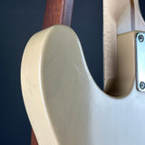 Close-up of the rear body corner of an electric guitar with a cream-colored finish, showing the edge of the neck, wood grain, and a silver hardware plate against a dark background.