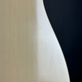 Close-up of a curved, light-colored wooden surface with visible scratches, set against a dark black background.
