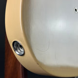 Close-up detail of a cream-colored guitar body showing a chrome 1/4-inch jack plug and a small screw terminal, with visible surface scratches.