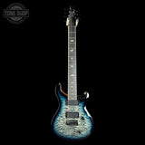 A double-cutaway electric guitar with a blue and black flame maple top, shown vertically against a solid black background. A Tone Shop watermark is visible in the top-left corner.