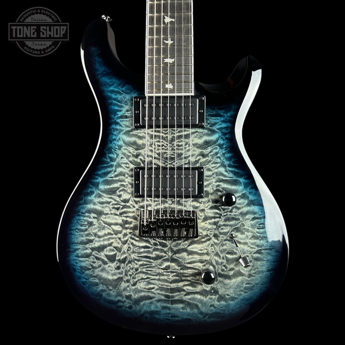 A close-up of an electric guitar body with a blue and black flamed maple finish, featuring black humbucker pickups and chrome hardware, set against a solid black background.
