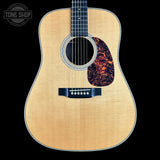 Acoustic guitar with a flame maple top on a black background, featuring the Tone Shop logo.