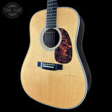 Acoustic guitar with a flame maple top on a black background, featuring the Tone Shop logo.