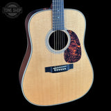 Acoustic guitar with a flame maple top on a black background, featuring the Tone Shop logo.