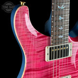 Close-up of a pink electric guitar with a black pickguard and gold hardware.