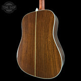 Back view of a wooden acoustic guitar with a visible brand logo in the corner.