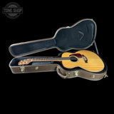 Acoustic guitar in a hard-shell case with 'Tone Shop' logo.