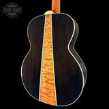 Acoustic guitar with a dark wood finish and visible grain pattern on a black background.