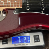A close-up of a glossy dark red electric guitar body resting on a digital scale displaying 7.127 oz.