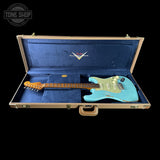 A turquoise blue Fender Stratocaster electric guitar resting inside an open vintage-style hard case with a blue velvet interior, shown against a solid black background.