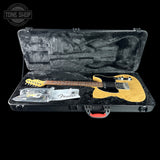 A natural wood Fender electric guitar inside an open black hard case with a black plush interior, shown on a black background. A Fender logo tag is visible on the headstock, and a Fender warranty card is placed in the case along with some accessories.