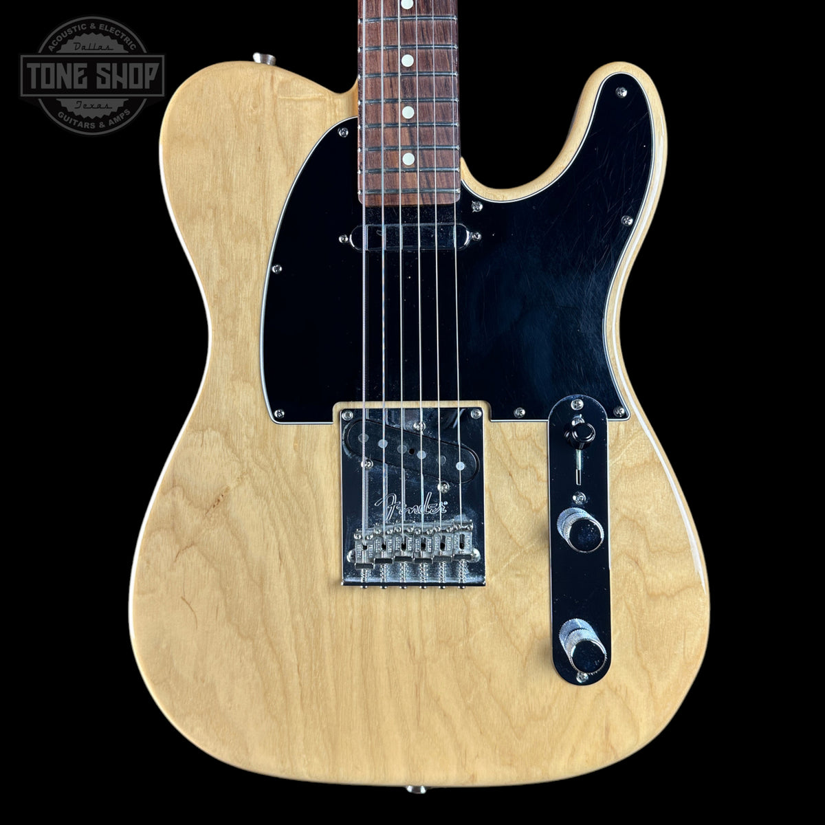 A natural wood electric guitar with a black pickguard and chrome hardware, shown against a solid black background with a Tone Shop watermark in the top left corner.