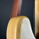 Close-up of a glossy light wood guitar body corner with a small chip on the finish, against a dark background.