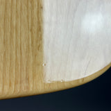 Close-up of a curved wooden object showing a light natural wood grain edge and a smooth pale beige surface, photographed against a dark navy background.