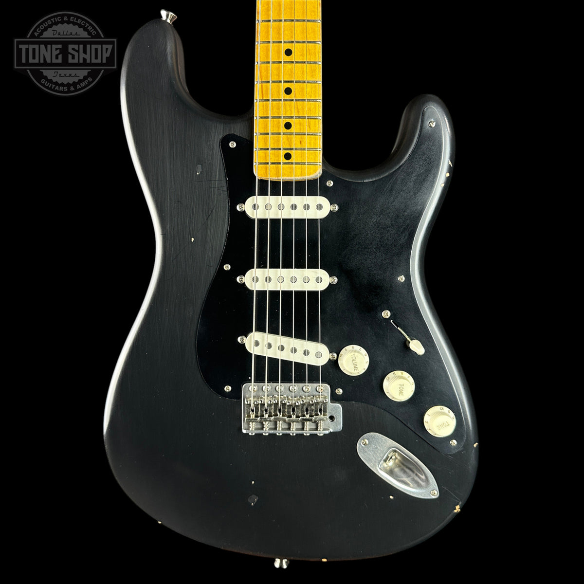 A black electric guitar with a yellow maple neck, featuring a black pickguard, cream-colored knobs and bridge, and a chrome headstock cover, shown against a black background with a Tone Shop logo in the top left corner.