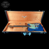 A blue electric guitar resting inside an open black hard case with a tan interior, photographed against a solid black background. A Tone Shop watermark is visible in the top-left corner.