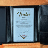 A Fender authenticity certificate insert displayed inside an open black leather portfolio folder, with tan textured paper backing visible around the edges.