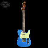 A blue electric guitar with a cream pickguard and brown wood headstock, shown against a solid black background with a Tone Shop watermark in the top left corner.