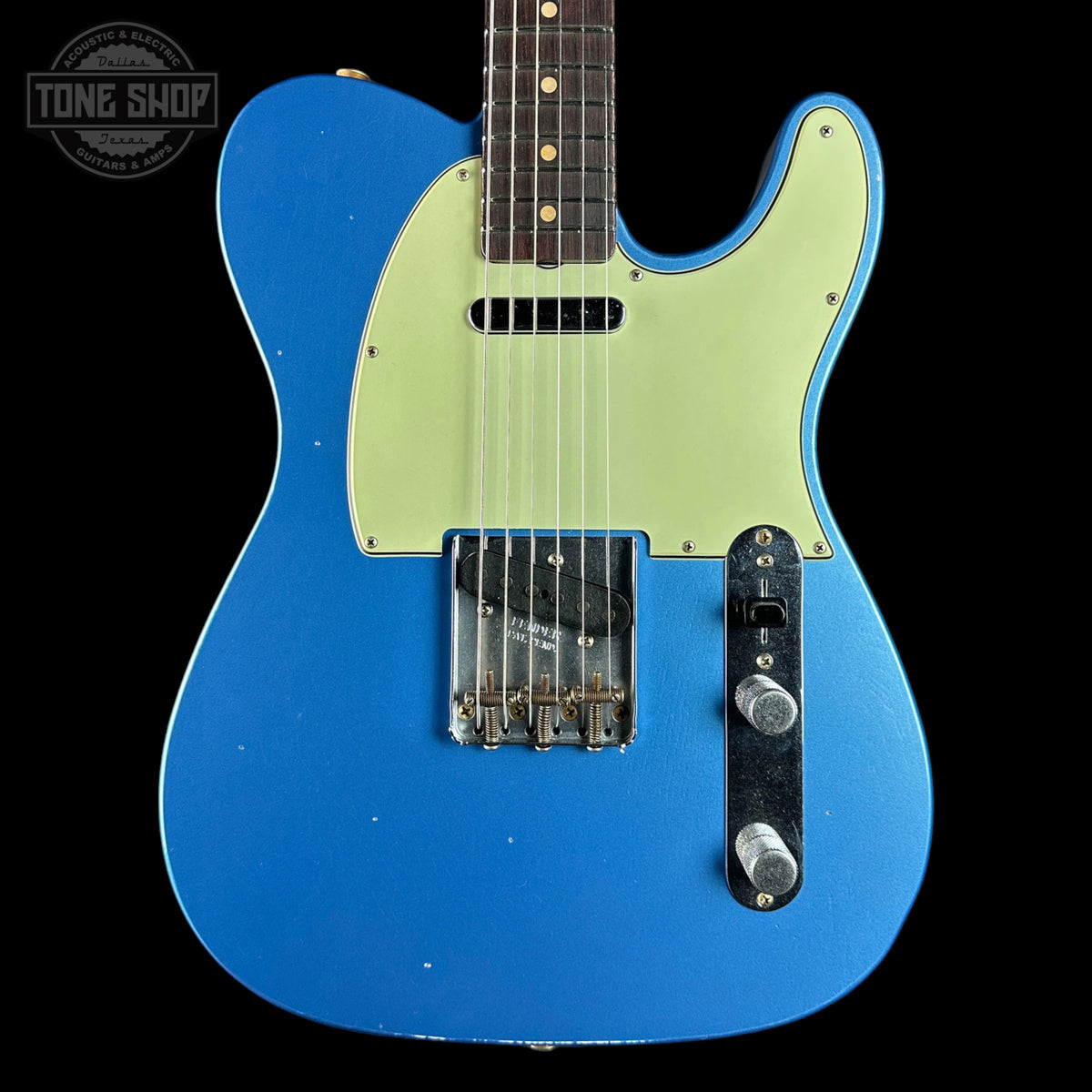 A blue electric guitar with a pale yellow-green pickguard, shown against a black background. A Tone Shop watermark is visible in the top left corner.