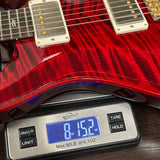 Red electric guitar on a digital scale displaying weight