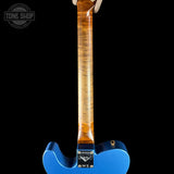Close-up of the back of a blue electric guitar body with a natural wood neck, held against a black background. A Tone Shop watermark is visible in the top left corner.