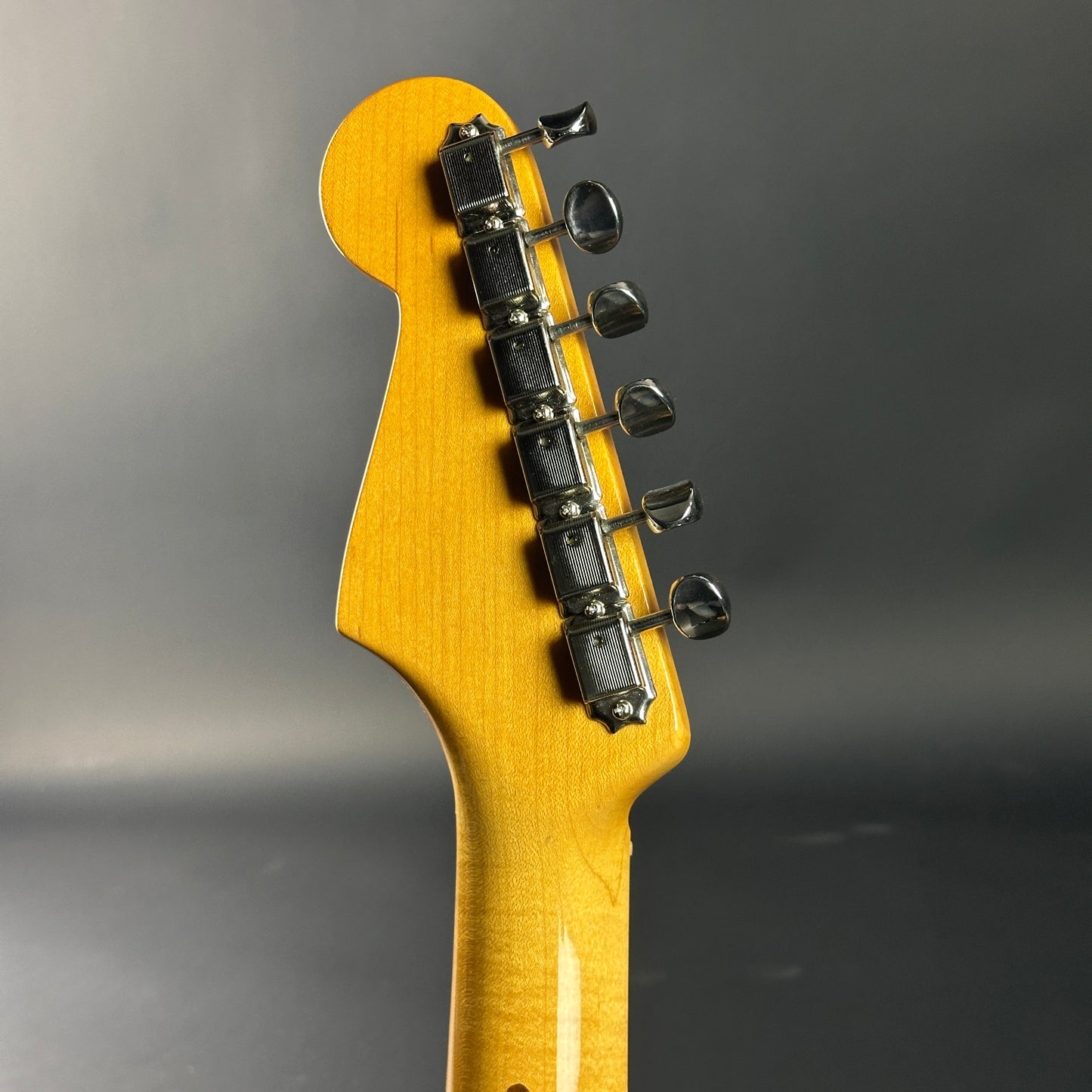 Close-up of a guitar headstock with tuning pegs on a dark background