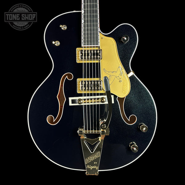 Black electric guitar with gold hardware on a black background, featuring the 'Tone Shop' logo.