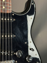 Close-up of a black electric guitar with control knobs on a dark background