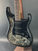 Black electric guitar with intricate design on the body against a gray background