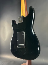 Black electric guitar body on a reflective surface with a neutral background