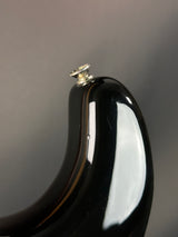 Close-up of a black guitar neck with a white pickguard on a gray background