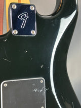 Close-up of a black guitar body with a visible brand logo on a gray background