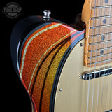 Close-up of a guitar with a colorful swirl design on a black background, featuring the Tone Shop logo.