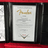 Fender certificate of authenticity in a black leather holder on a red surface